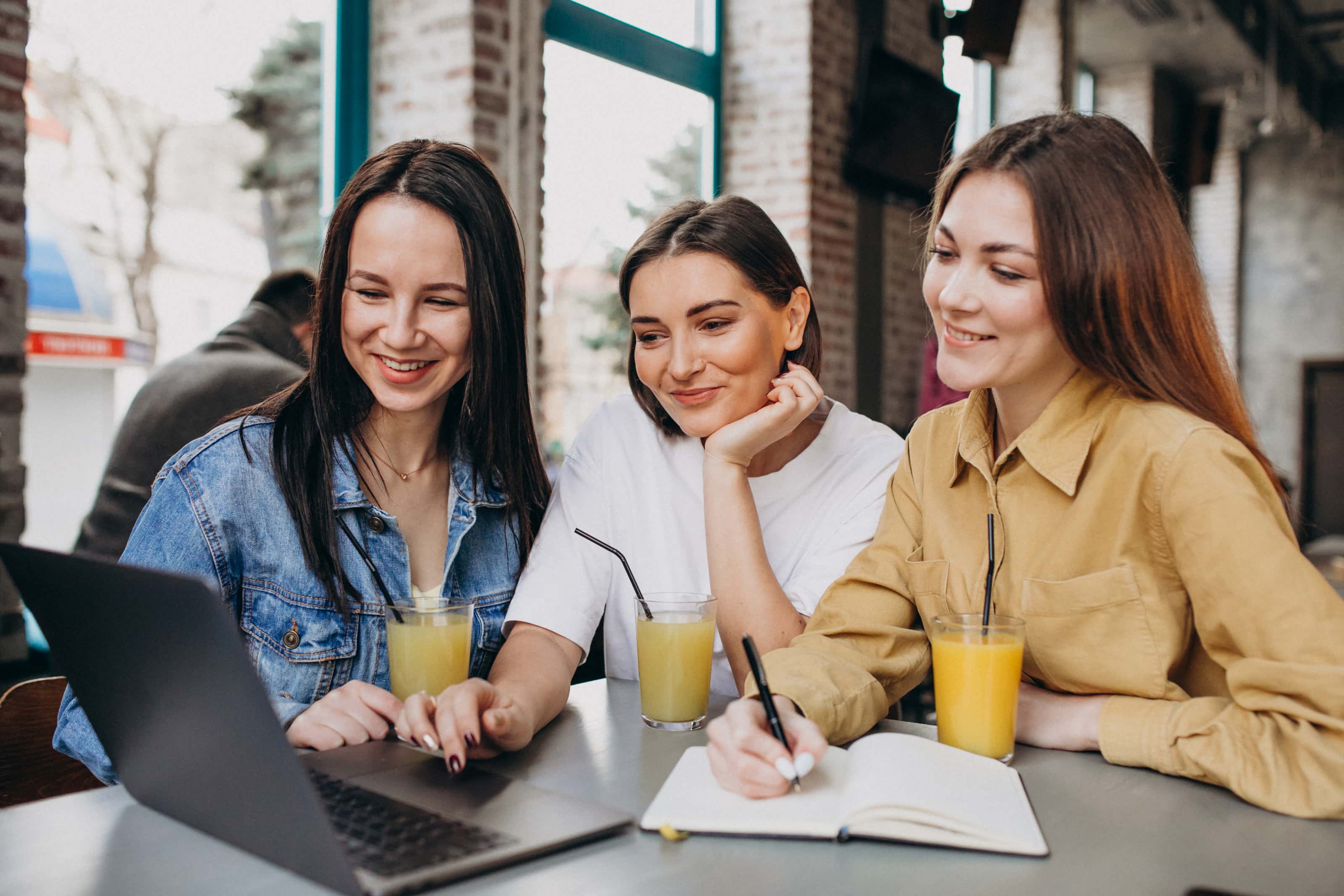 Three students preparing exam with laptop cafe